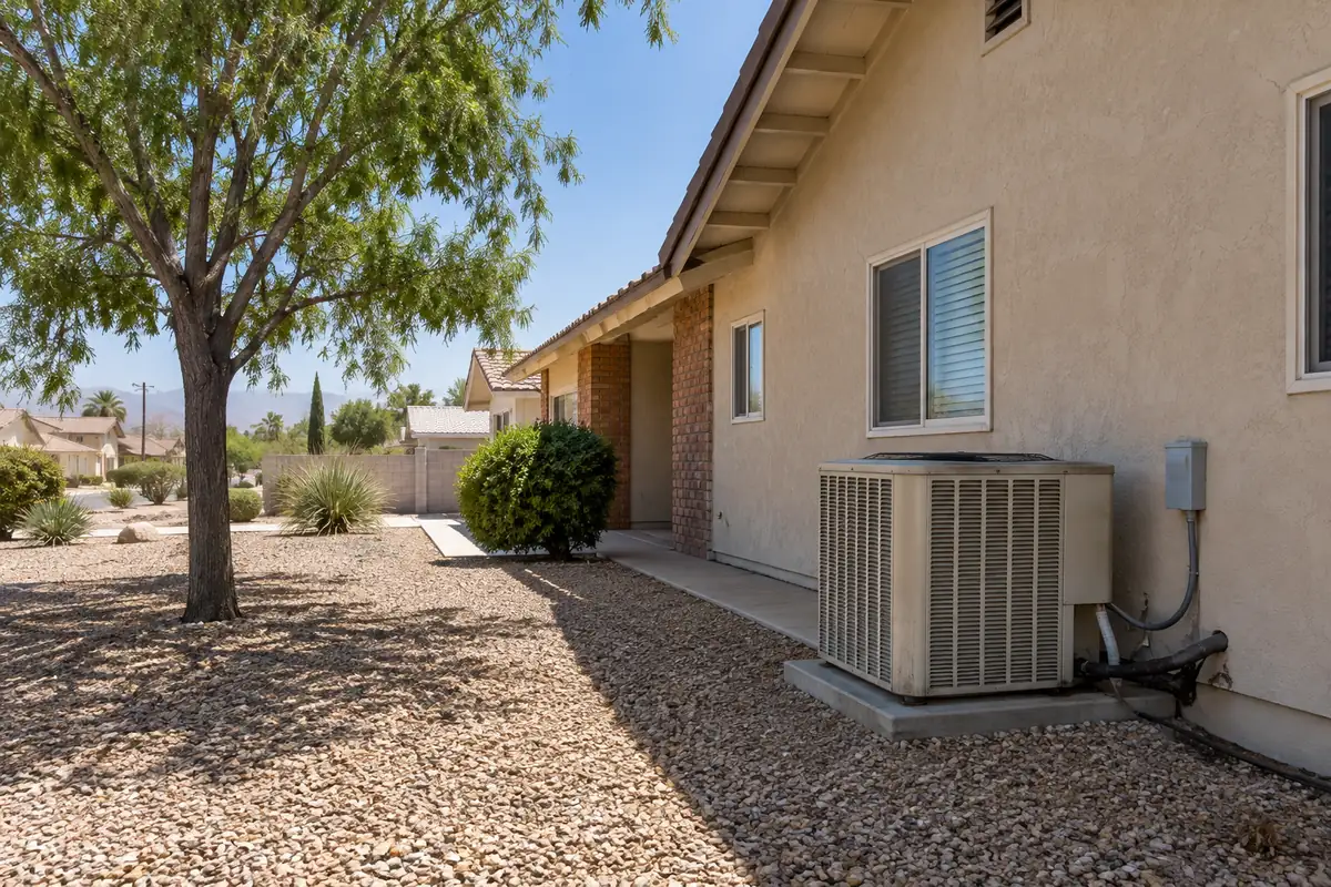 Condenser on a gravel yard beside a one-story house and a shade tree, ac replacement in Las Vegas, NV